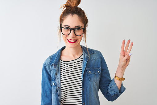 Redhead woman wearing striped t-shirt denim shirt and glasses over isolated white background showing and pointing up with fingers number three while smiling confident and happy.