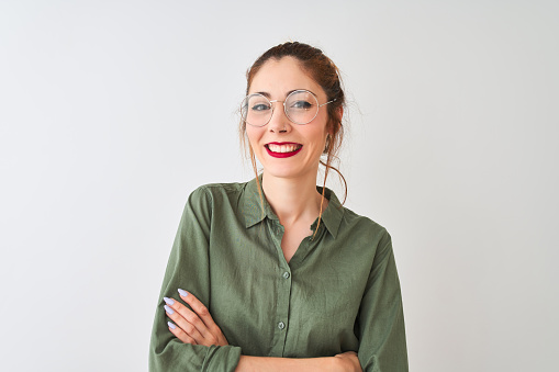 Redhead woman wearing green shirt and glasses standing over isolated white background happy face smiling with crossed arms looking at the camera. Positive person.