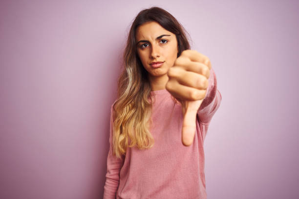 Young beautiful woman wearing a sweater over pink isolated background looking unhappy and angry showing rejection and negative with thumbs down gesture. Bad expression. Young beautiful woman wearing a sweater over pink isolated background looking unhappy and angry showing rejection and negative with thumbs down gesture. Bad expression. thumbs down stock pictures, royalty-free photos & images