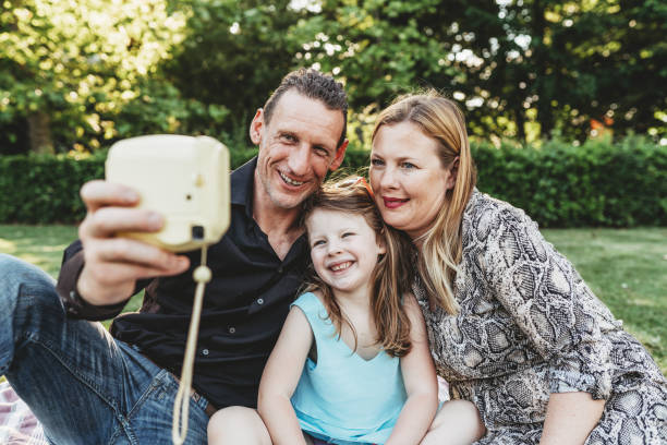 glückliche familie im park mit einem selfie zusammen mit einer instant-print-kamera - instant print transfer stock-fotos und bilder