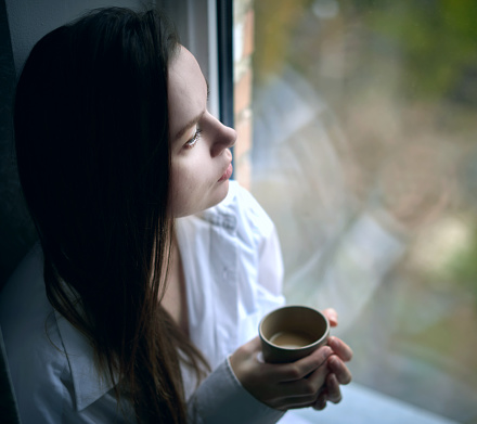 pretty young woman sitting sad near the window with cup of coffee