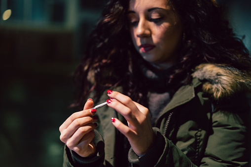 Young adult woman rolling a cigarette outdoor in the city at night