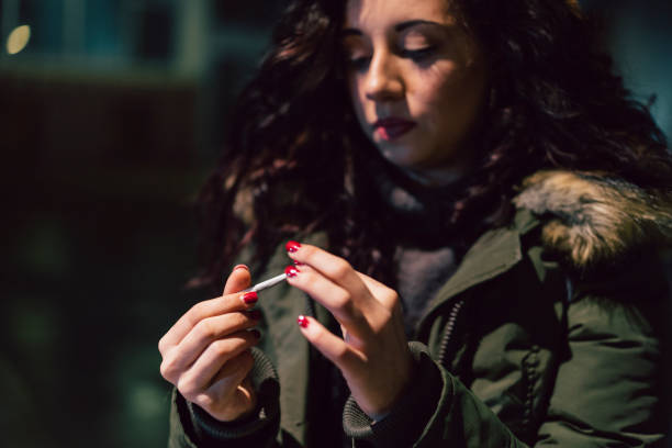 young adult woman rolling a cigarette outdoor in the city at night - cigarette wrapping imagens e fotografias de stock