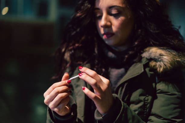 молодая взрослая женщина прокатки сигареты на открытом воздухе в городе в ночное время - cigarette wrapping стоковые фото и изображения