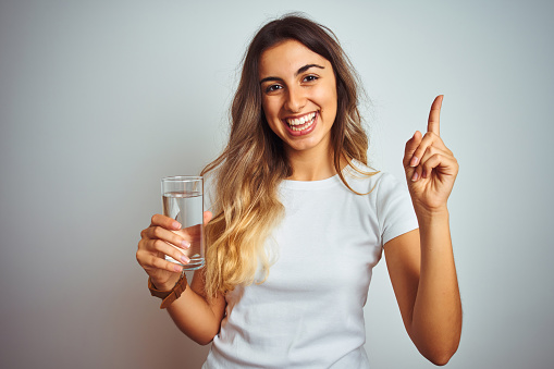 Young beautiful woman drinking a glass of water over white isolated background very happy pointing with hand and finger to the side