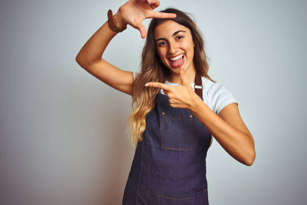 istock Young beautiful woman wearing apron over grey isolated background smiling making frame with hands and fingers with happy face. Creativity and photography concept. 1167936992