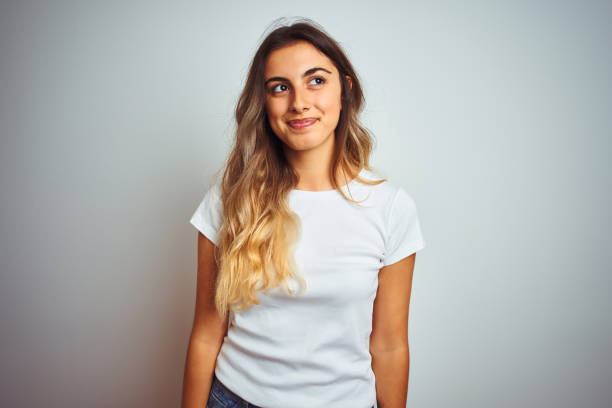 young beautiful woman wearing casual white t-shirt over isolated background smiling looking to the side and staring away thinking. - mannered imagens e fotografias de stock