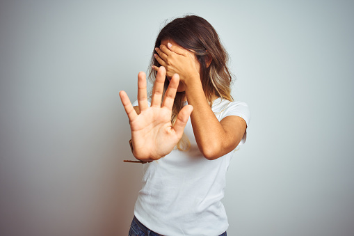 Young beautiful woman wearing casual white t-shirt over isolated background covering eyes with hands and doing stop gesture with sad and fear expression. Embarrassed and negative concept.