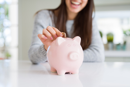 Young woman smiling putting a coin inside piggy bank as savings for investment