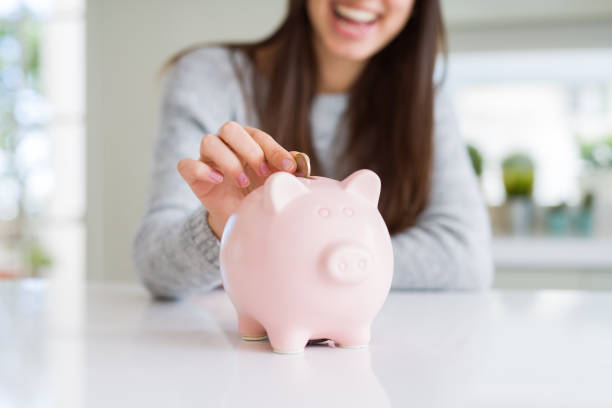 молодая женщина улыбается положить монету в копилку в качестве сбережений для инвестиций - beautiful pink business finance стоковые фото и изображения