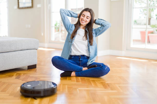 istock Young woman using automatic vacuum cleaner to clean the floor, controling machine housework robot 1167939817