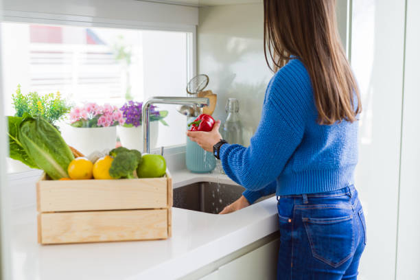 istock Young woman washing vegetables and fruit using water from sink 1167939900