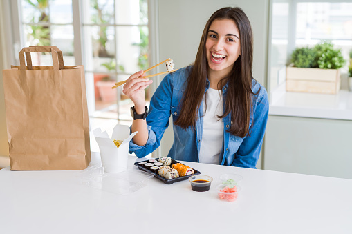 Young woman eating sushi asian food and noodles using choopsticks from take away delivery