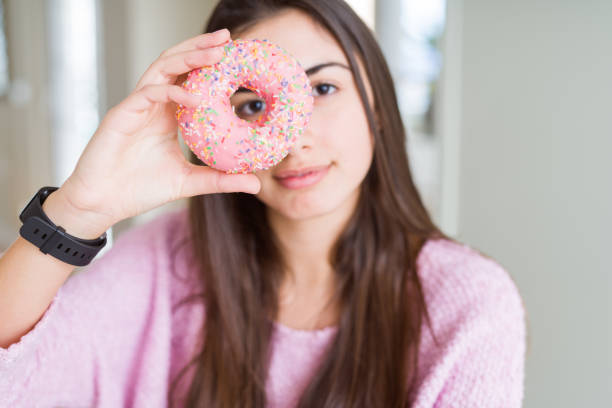 istock Beautiful young woman eating pink chocolate chips donut with a confident expression on smart face thinking serious 1167941180