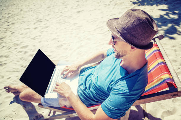 istock Attractive young man with laptop working on the beach. Freedom, remote work, freelancer, technology, internet, travel and vacation concepts 1167941507