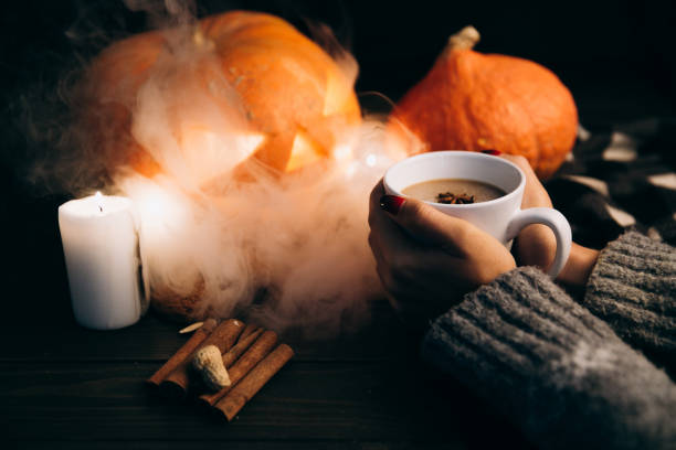 Woman holds a cup of hot chocolate in her arms before a Halloween pumpkin covered with white smoke Woman holds a cup of hot chocolate in her arms before a Halloween pumpkin covered with white smoke gross coffee stock pictures, royalty-free photos & images