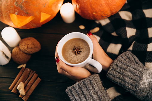 Woman holds a cup of hot chocolate in her arms before a Halloween pumpkin