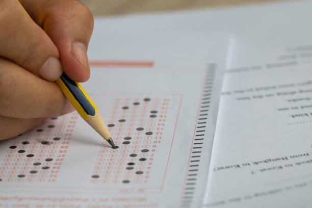 istock School or university students hands taking exams, writing examination room with holding pencil on optical form answers paper sheet on desk doing final test in classroom. Education assessment Concept 1167947013