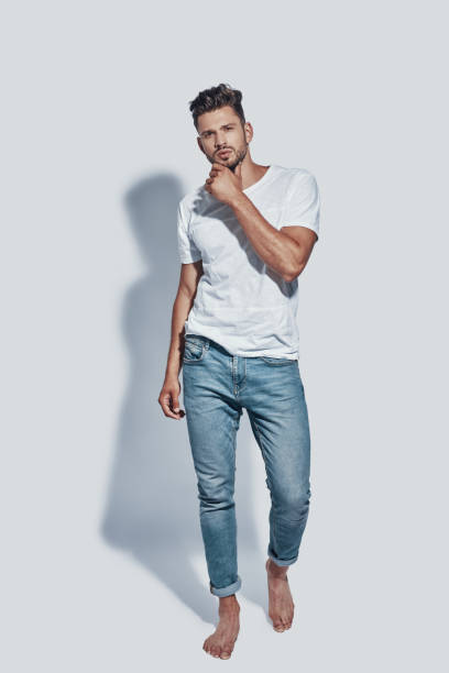 Full length of handsome young man looking at camera while standing against grey background