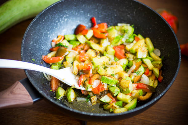 fried zucchini with red pepper, onions, tomatoes and other vegetables in a pan