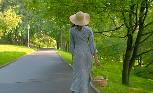 Romantic woman with basket in her hand walking in the park. Rear view