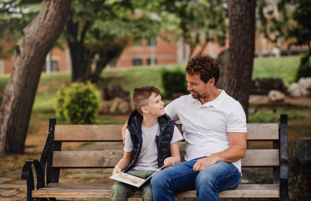 istock Father with son sitting on bench outdoors in town, reading a book. 1167963321
