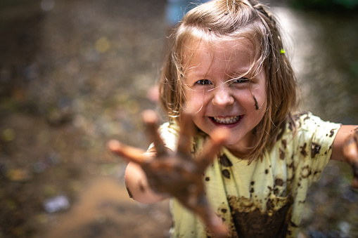 Portrait of smiling girl playing with mud in forest.