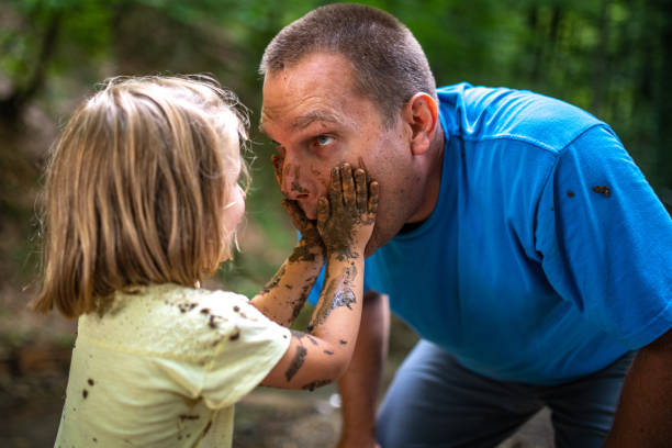Father and daughter playing with mud in forest stock photo
