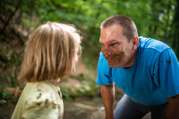 Smiling father and daughter playing with mud in forest.