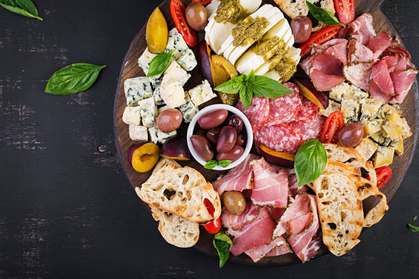 Antipasto platter with ham, prosciutto, salami, blue cheese, mozzarella with pesto and olives on a wooden background. Top view, overhead stock photo