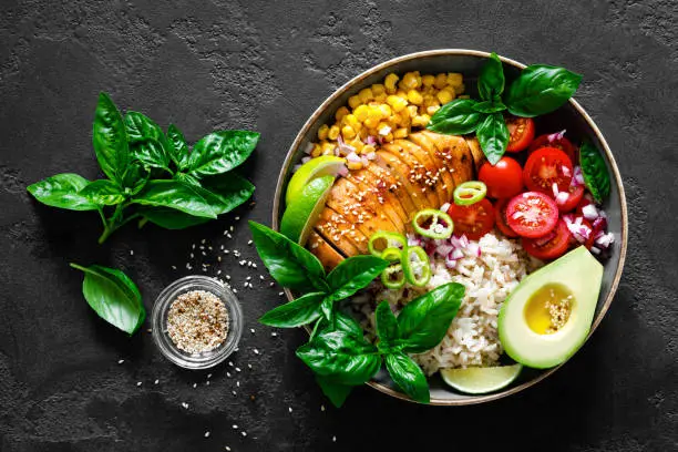 Grilled chicken breast lunch bowl with fresh tomato, avocado, corn, red onion, rice and basil