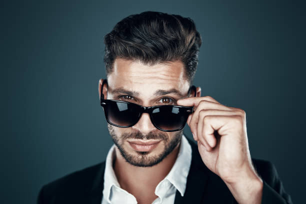 istock Charming young man in formalwear adjusting eyewear and looking at camera while standing against grey background 1167967054