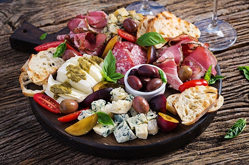 Antipasto platter with ham, prosciutto, salami, blue cheese, mozzarella with pesto and olives on a wooden background.