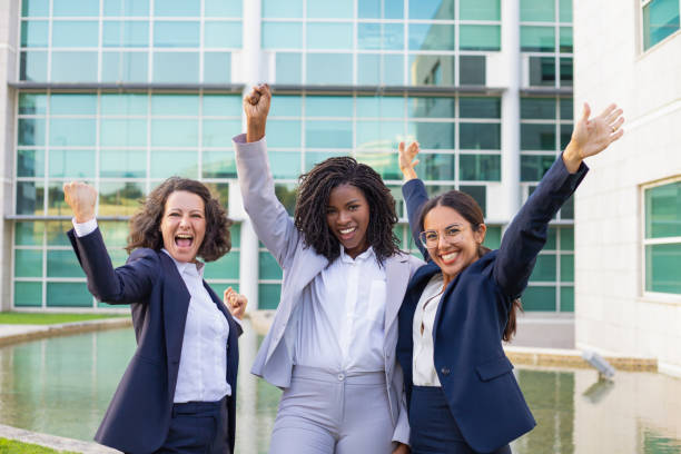 mujeres de negocios felices y emocionadas que se regocijen ante el éxito corporativo - three people group of people standing business person fotografías e imágenes de stock