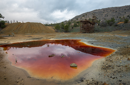 Abandoned copper mine with red toxic water and dramatic stormy cloudy sky at Mitsero area in Cyprus