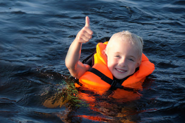 Happy blond little girl swimming in orange life jacket in the sea. girl shows thumb up stock photo