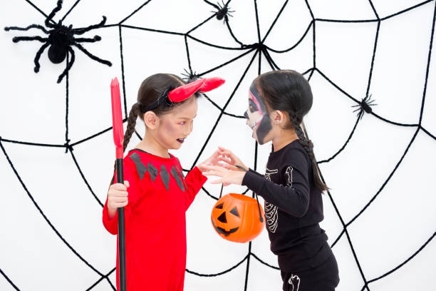Little girl in halloween costume tease each other cheerfully. Little girl in halloween carnival costume is holding jack-o-lantern (pumpkin) and trident. Asian cute children tease each other cheerfully in front of the backdrop decorated with spiderwebs. skeloton hand stock pictures, royalty-free photos & images