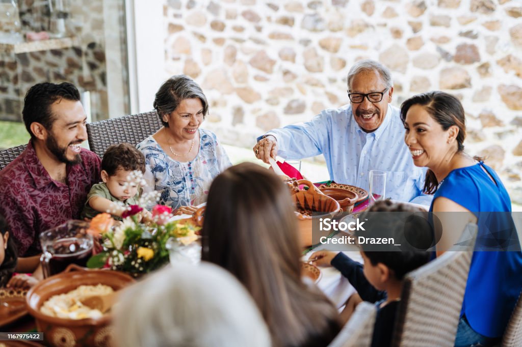 Latin senior man serving the food to his family at dinner table Three generation family at lunch Family Stock Photo