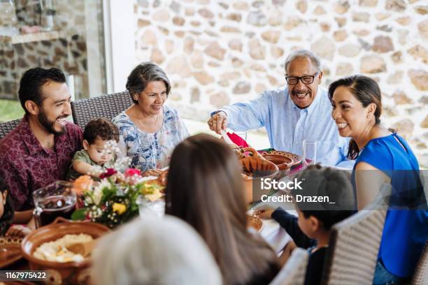 Latin Senior Man Serving The Food To His Family At Dinner Table Stock Photo - Download Image Now