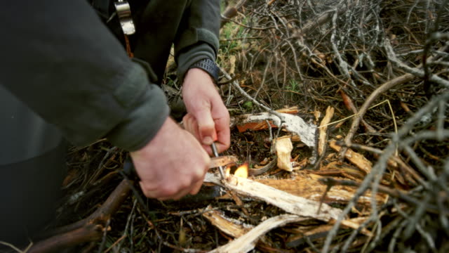 Male wilderness survival expert lighting a fire on a clearing in the forest