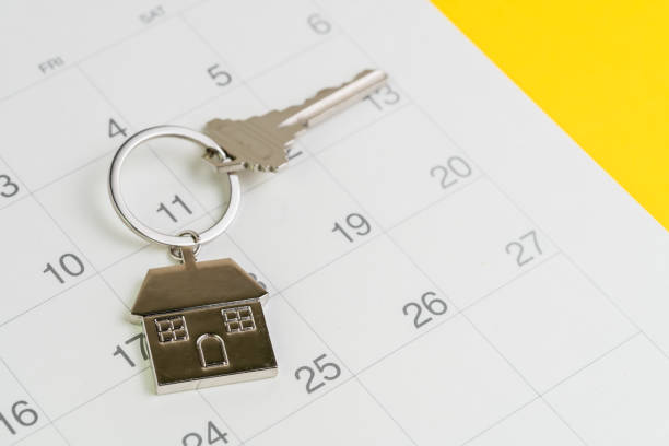 Reminder to pay for mortgage, schedule event or real estate payment day, silver house keyring on white clean calendar, yellow background stock photo