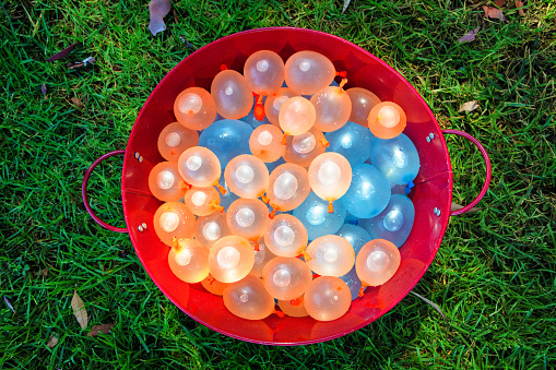 Bucket of colorful water balloons on lawn
