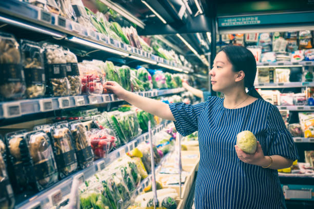 Asian pregnant woman grocery shopping at the vegetable aisle in supermarket stock photo