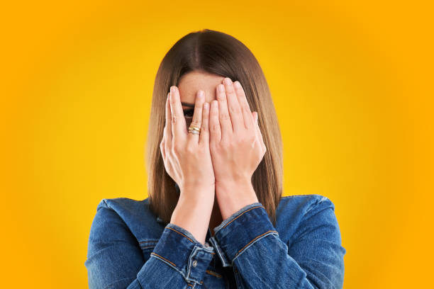 femme malheureux dans la veste de denim au-dessus du fond jaune - mains devant les yeux photos et images de collection