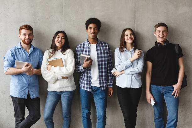 College students with books smiling to camera over grey wall College students with books smiling to camera over grey wall, having break adult education book stock pictures, royalty-free photos & images