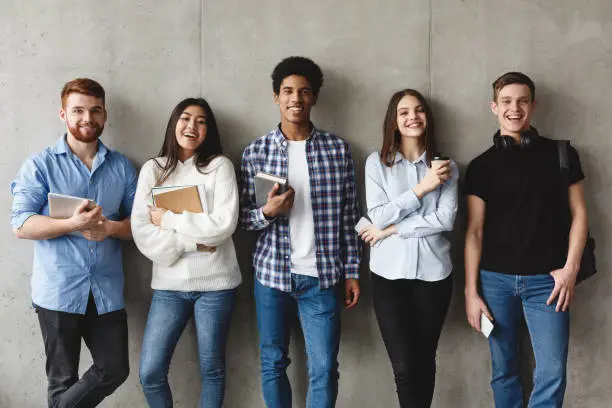 Photo of College students with books smiling to camera over grey wall
