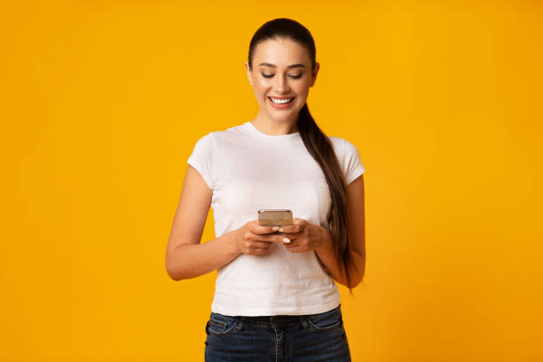 istock Joyful Girl Chatting With Friends Using Cellphone On Yellow Background 1167993234