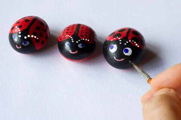 Photo of hand painting three stones as cute ladybugs on white paper