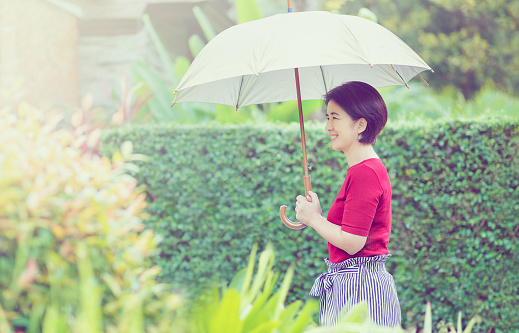 Middle age Asian woman holding umbrella in strong sunlight