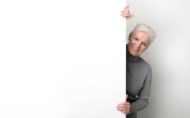 istock Beautiful senior woman hiding behind big white empty board 1168000344